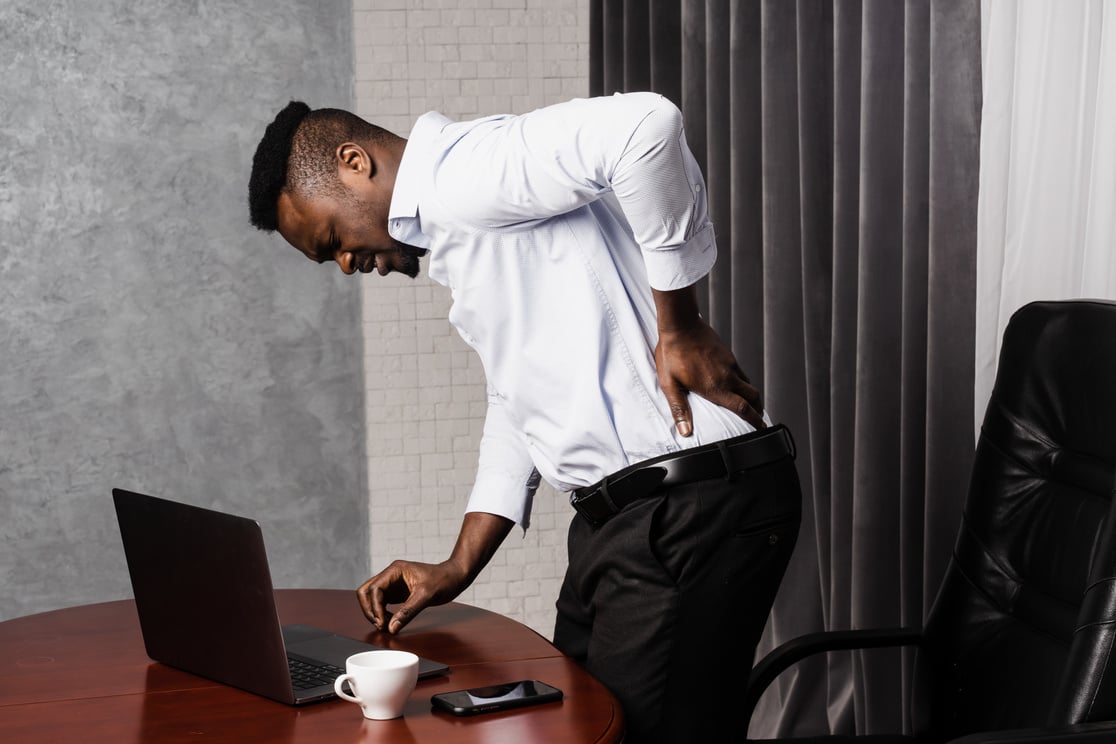 Cervical spine osteochondrosis is radicular syndromes of african american man. African manholds his back and feels pain in his back and neck after working for long hours with laptop online in office.